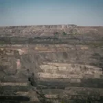 Tambang terbuka berskala besar dengan lapisan batuan mineral dan langit biru cerah